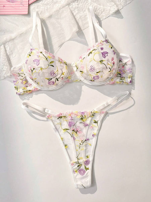 Conjunto de lencería floral bordado blanco visto desde arriba sobre una superficie texturizada.