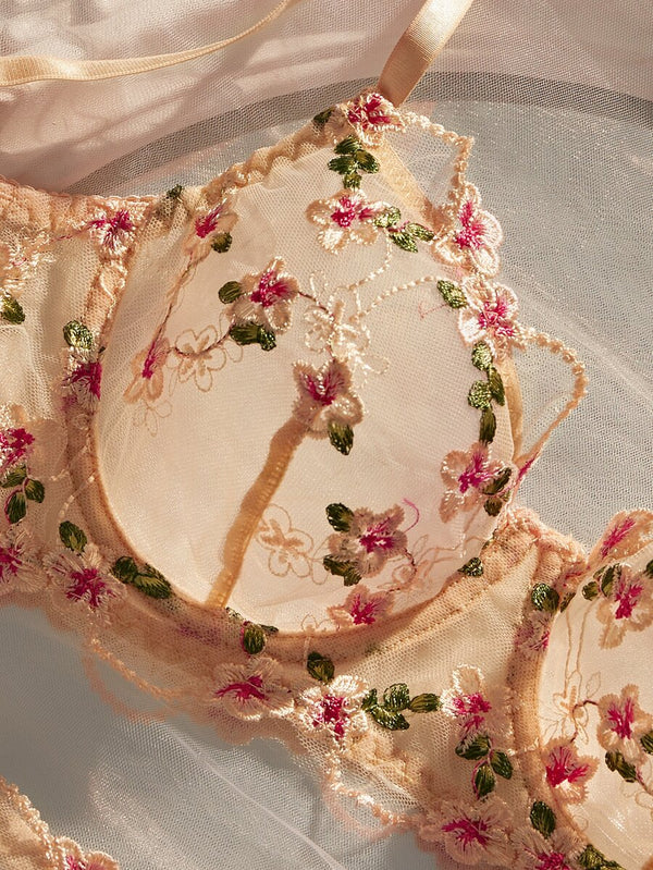 Detalle del bordado floral en tonos rosa y verde sobre malla nude