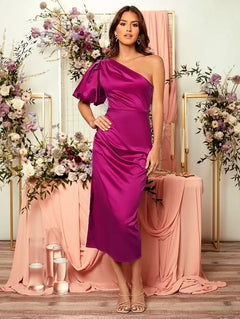 Mujer posando con vestido asimétrico magenta satinado y manga abullonada en un entorno decorado con flores.