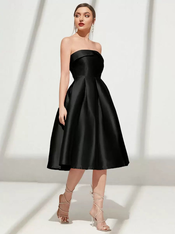 Detalle de la falda midi plisada de un vestido de fiesta negro y los pies de la modelo con tacones.