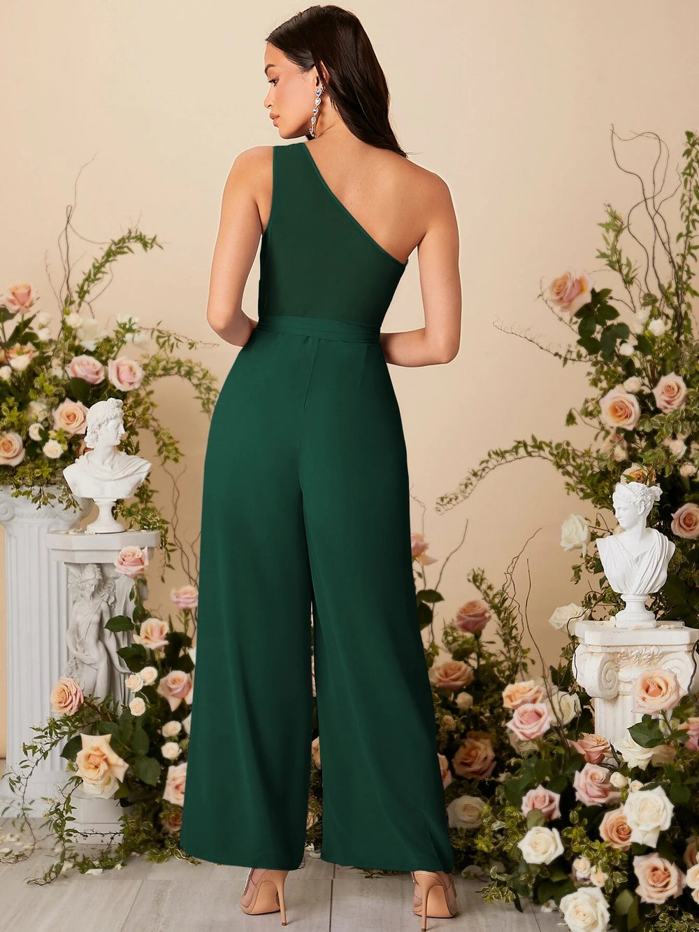 Modelo con mono largo verde oscuro elegante con cuello asimétrico y cinturón.