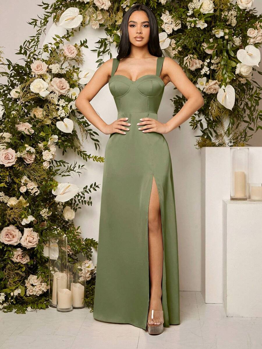 Mujer modelando un vestido largo elegante de color verde olivo con tirantes anchos, escote corazón, y una abertura alta en la pierna, posando frente a un arco de flores.
