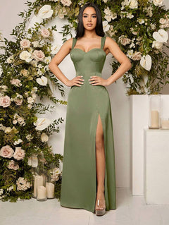 Mujer modelando un vestido largo elegante de color verde olivo con tirantes anchos, escote corazón, y una abertura alta en la pierna, posando frente a un arco de flores.