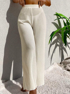 Vista de perfil de las piernas anchas del pantalón blanco crudo con el mar de fondo.