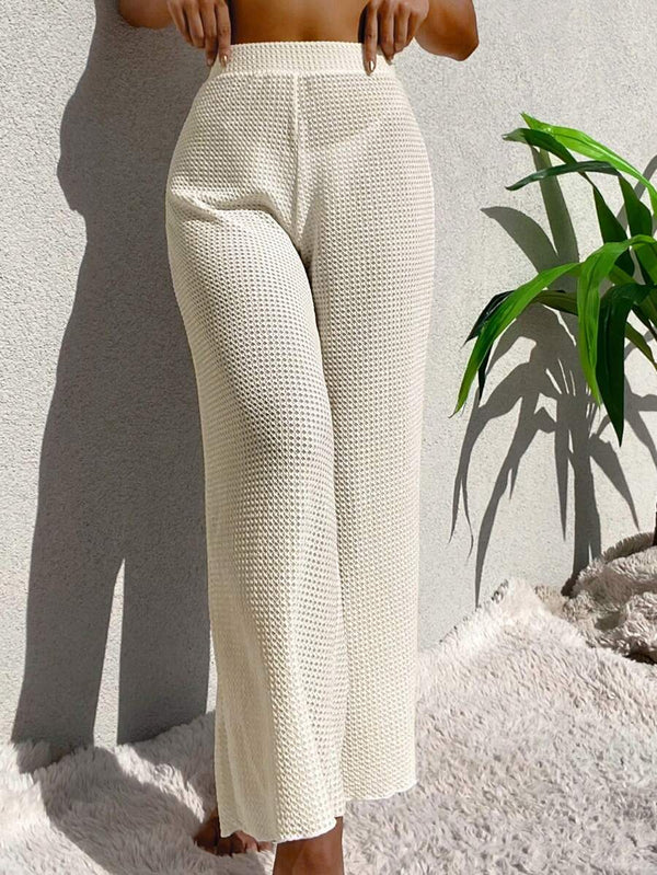 Vista de perfil de las piernas anchas del pantalón blanco crudo con el mar de fondo.