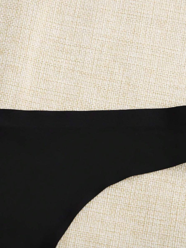 Composición de lencería básica con tres tangas negras invisibles junto a flores decorativas.