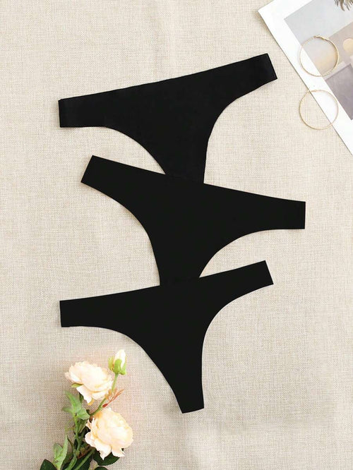 Tres tangas de color negro sin costuras dispuestas sobre una superficie de tela beige.