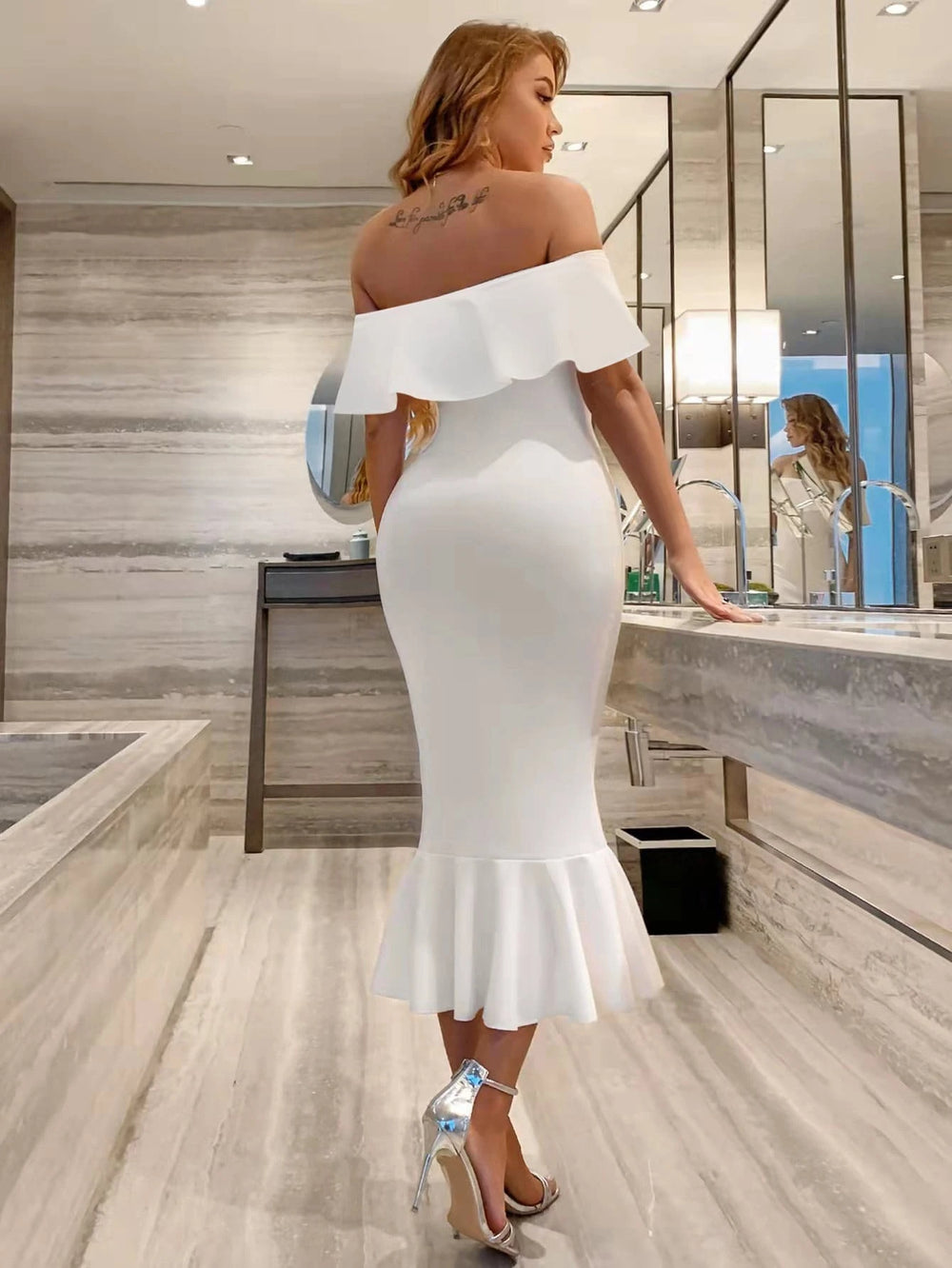Vestido blanco elegante con volante, mostrando el escote de hombros descubiertos y corte sirena.