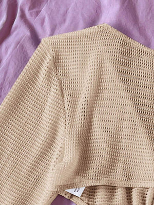 Vista lateral del vestido corto beige mostrando la textura del tejido y el corte ajustado.