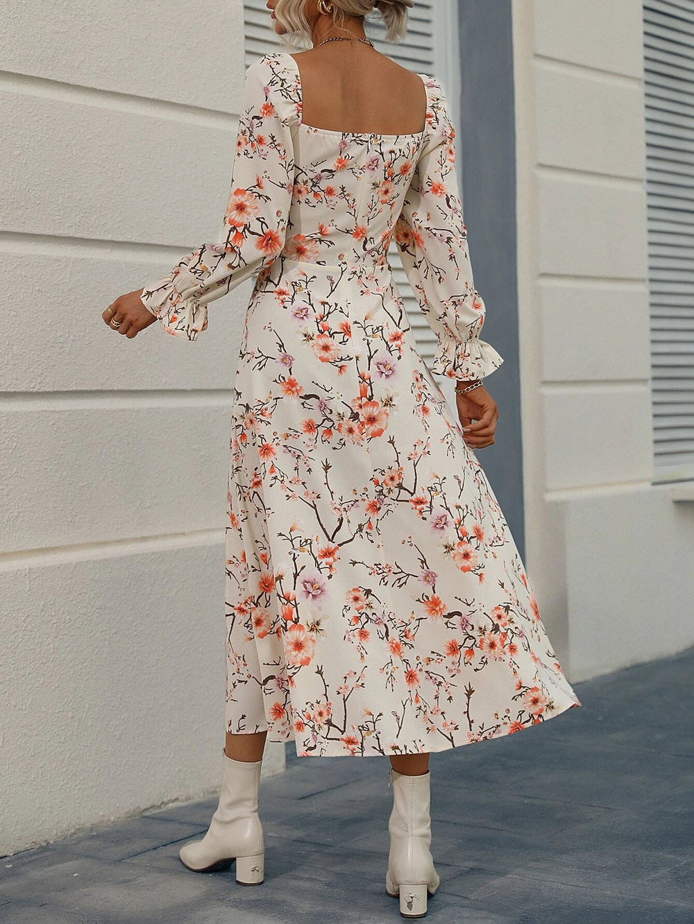 Mujer usando un vestido largo floral con abertura, mangas largas y escote cuadrado, combinándolo con botas blancas.