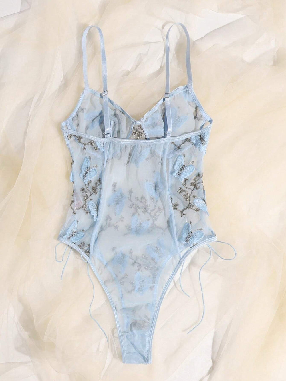 Vista frontal del body celeste romántico-floral bordado con transparencias y lazos laterales.