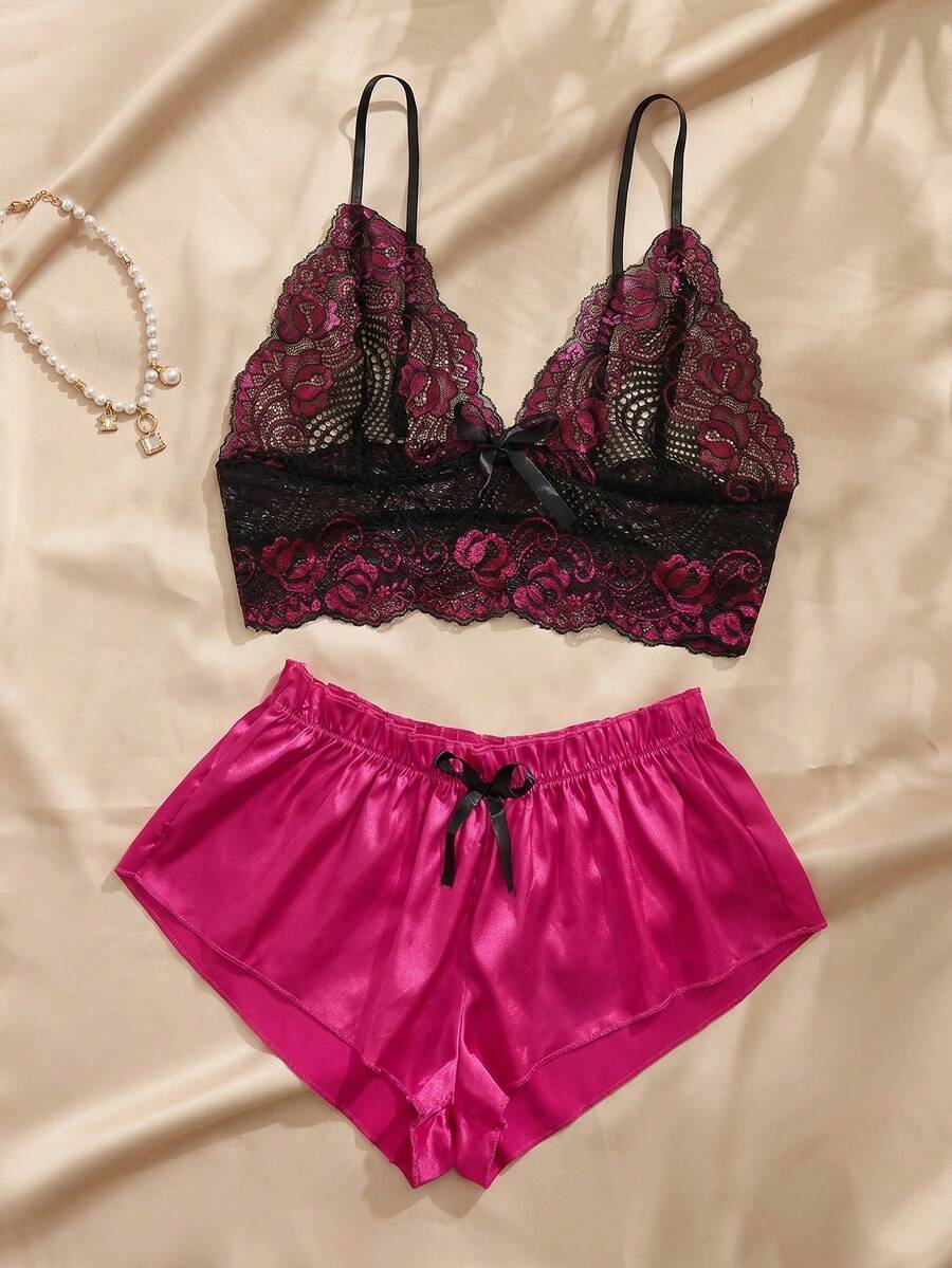 Conjunto de pijama de encaje fucsia y negro con short de satén fucsia sobre un fondo de tela satinada.