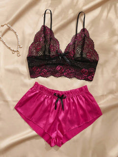 Conjunto de pijama de encaje fucsia y negro con short de satén fucsia sobre un fondo de tela satinada.