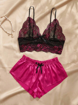 Conjunto de pijama de encaje fucsia y negro con short de satén fucsia sobre un fondo de tela satinada.