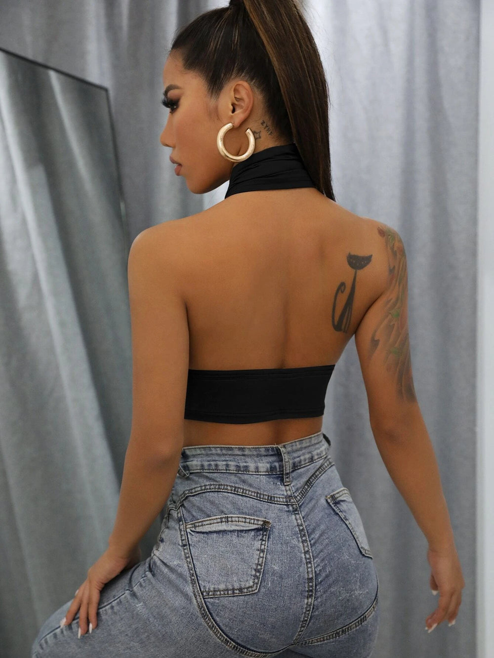 Modelo luciendo un top negro halter cruzado con jeans