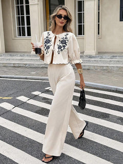 Mujer con estilo caminando por la calle con un conjunto de dos piezas color crema con bordado floral negro.