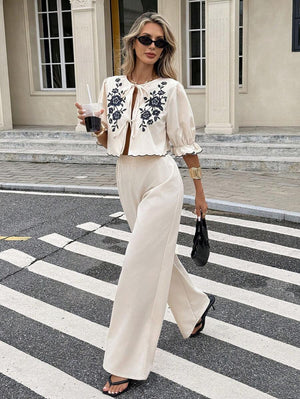 Mujer con estilo caminando por la calle con un conjunto de dos piezas color crema con bordado floral negro.