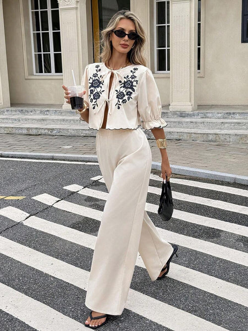 Mujer con estilo caminando por la calle con un conjunto de dos piezas color crema con bordado floral negro.