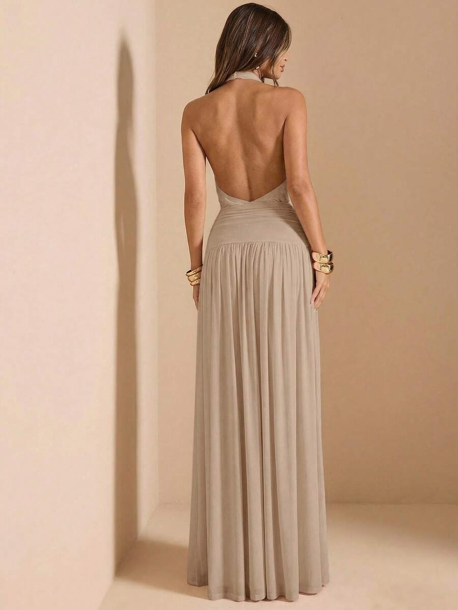 Vista completa de una mujer usando un vestido largo elegante color beige con cuello halter y abertura lateral.