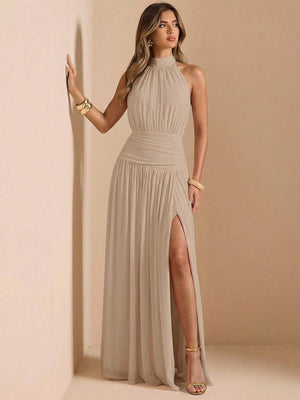 Una mujer de pie mostrando la abertura lateral de su vestido largo color beige y sandalias doradas.