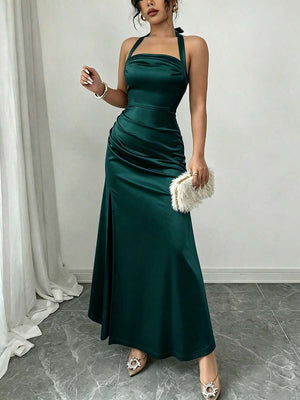 Mujer posando con un vestido de gala verde esmeralda de tejido satinado y abertura en la pierna.