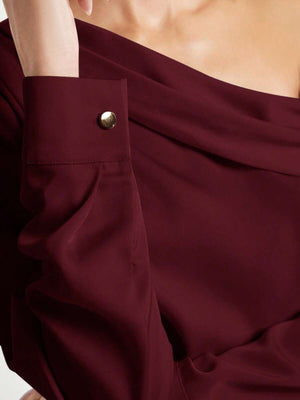Primer plano del cuello asimétrico y el detalle fruncido de una blusa color vino de manga larga.
