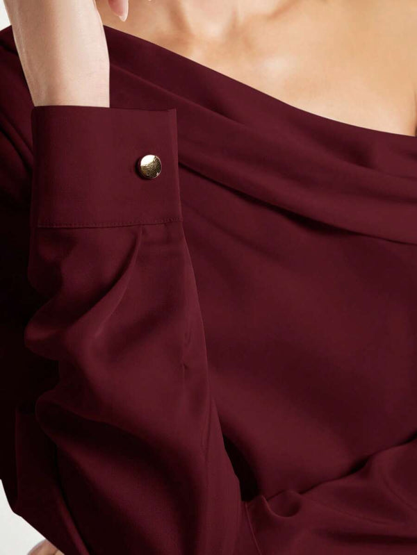 Primer plano del cuello asimétrico y el detalle fruncido de una blusa color vino de manga larga.