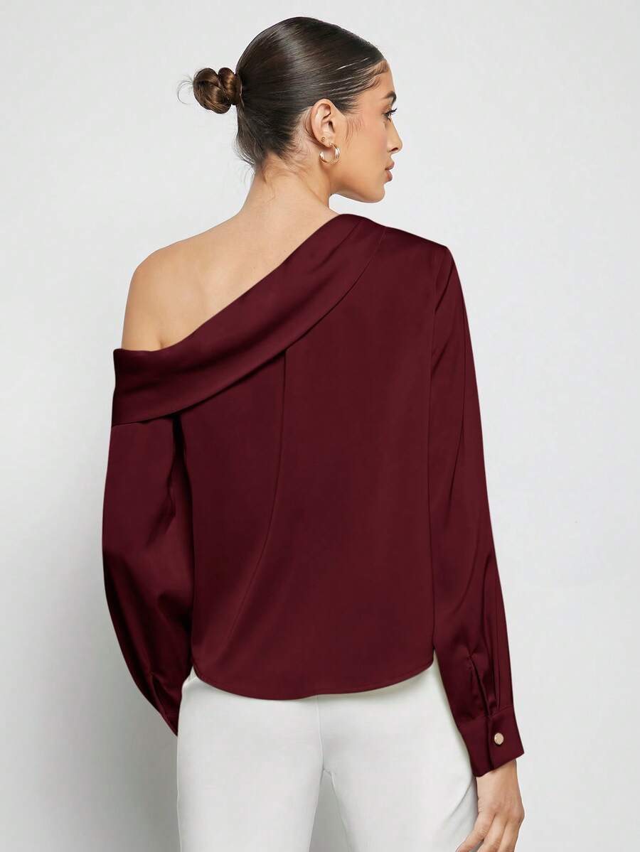 Mujer modelando una blusa elegante color burdeos con cuello asimétrico y hombro descubierto, combinada con pantalones blancos.