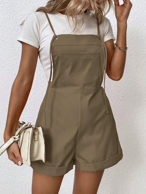 Mujer vistiendo un overall corto color marrón caqui sobre una camiseta blanca, sosteniendo un bolso blanco.
