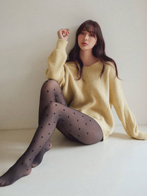 Modelo sentada luciendo medias negras con diseño de corazones.