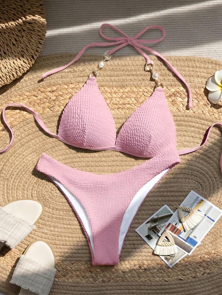 Vista completa de un bikini de dos piezas color rosa con textura sobre una estera de paja.