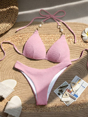 Vista completa de un bikini de dos piezas color rosa con textura sobre una estera de paja.