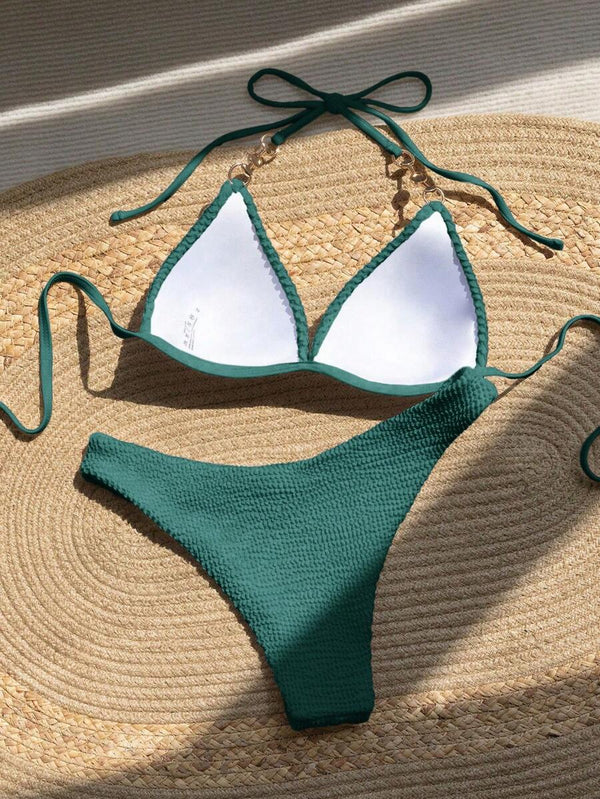 Detalle del top de bikini verde con tirantes halter y un adorno de perla y metal dorado.