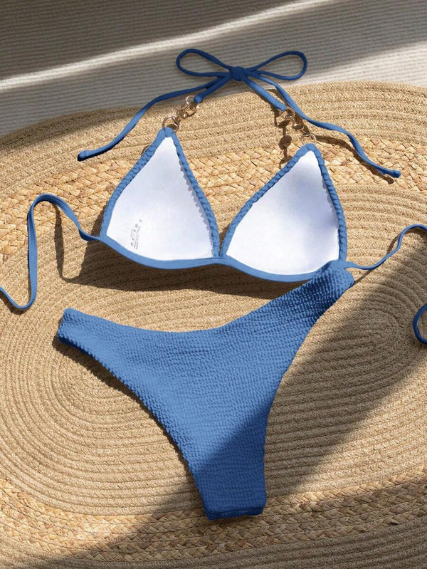 Detalle del top de bikini triangular azul con tirantes halter y un adorno de perla.