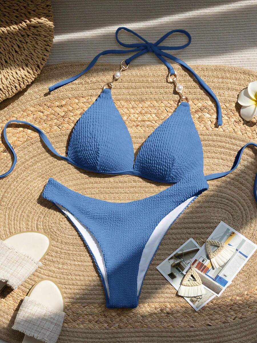 Bikini azul de dos piezas texturizado con detalles de perlas en los tirantes, visto desde arriba.
