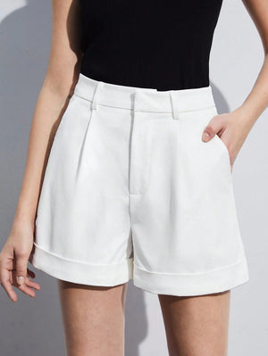 Detalle de las piernas de una modelo con shorts blancos, sandalias de tacón negras y un bolso.