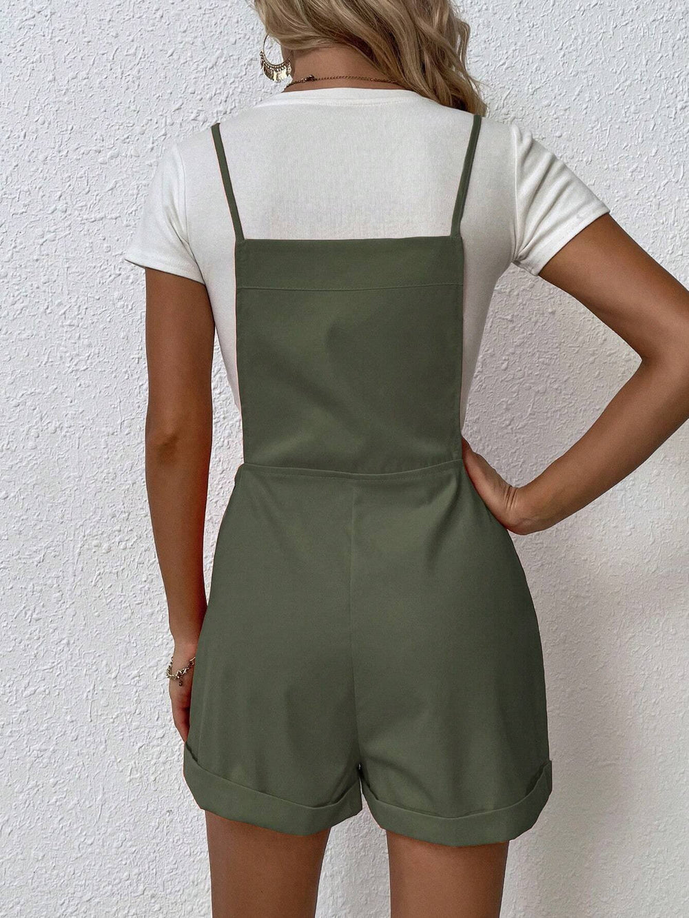 Mujer con overol corto con tirantes finos en color verde militar y blusa blanca.