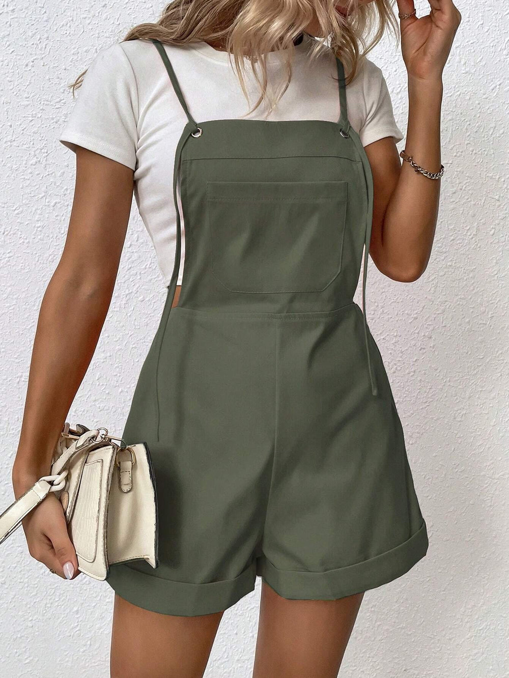 Mujer con overol corto con tirantes finos en color verde militar y blusa blanca.