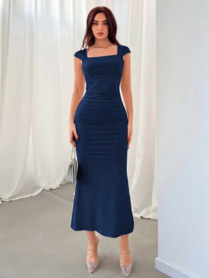 Mujer posando con un vestido midi azul marino de escote cuadrado y mangas casquillo.