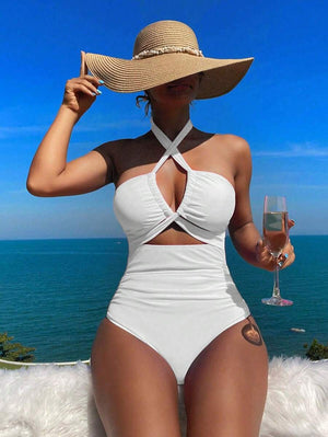Mujer vistiendo un traje de baño entero blanco con escote halter cruzado y sombrero de paja, posando frente al mar.
