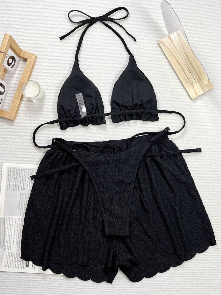 Mujer modelando un conjunto de playa negro de tres piezas con top halter y shorts texturizados.
