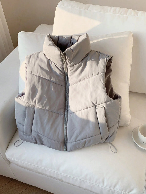 Chaleco gris claro acolchado sobre sillón blanco.