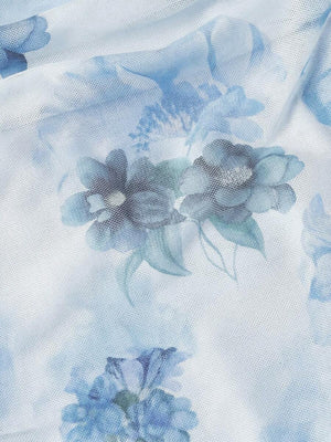 Detalle del bajo estilo sirena de un vestido midi floral azul claro, con la falda extendida sobre el césped.