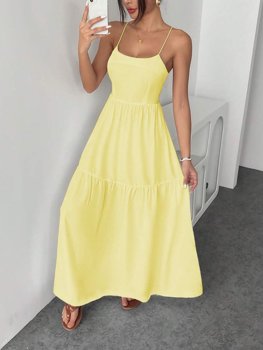Mujer luciendo un vestido largo amarillo vibrante con tirantes finos y falda de volantes.