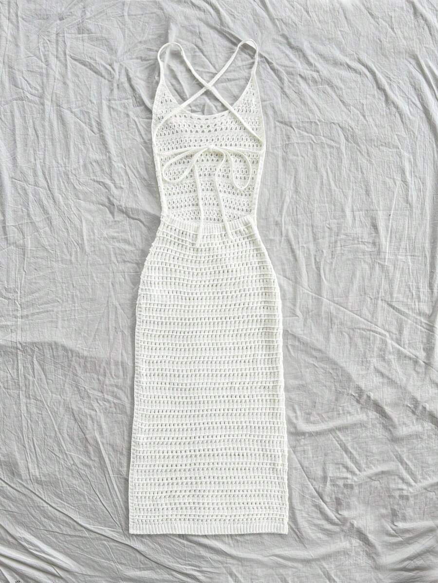 Vestido largo tejido de crochet blanco en un flat lay con sandalias, sombrero de paja y flores.