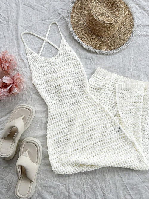Vestido largo tejido de crochet blanco en un flat lay con sandalias, sombrero de paja y flores.