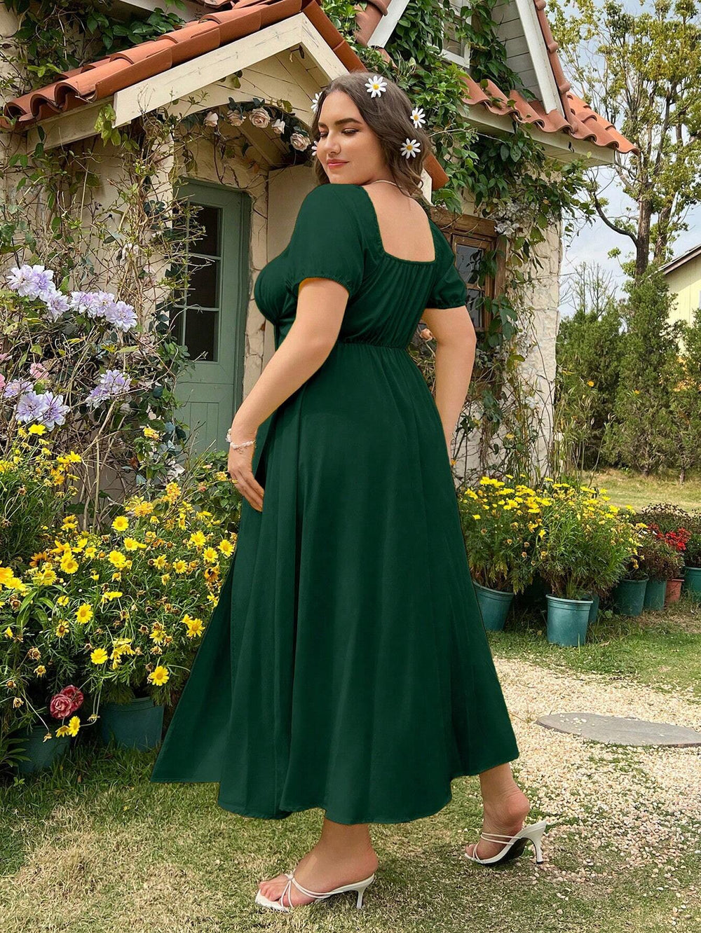 Mujer usando vestido verde oscuro midi con abertura alta frente al jardín.