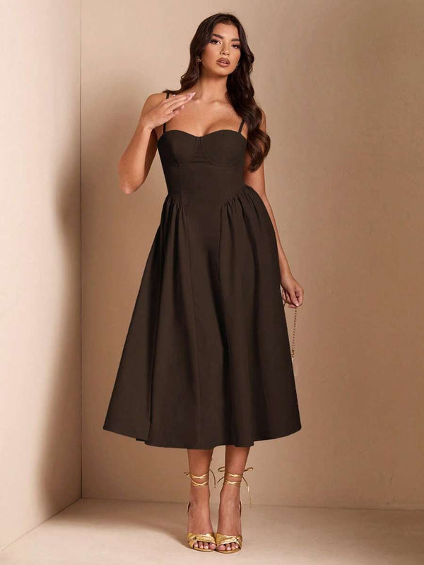 Detalle de una mujer con vestido midi café sosteniendo un bolso de mano y usando tacones dorados.