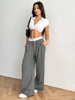 Detalle de cintura a rayas y pliegues frontales del pantalón gris claro.