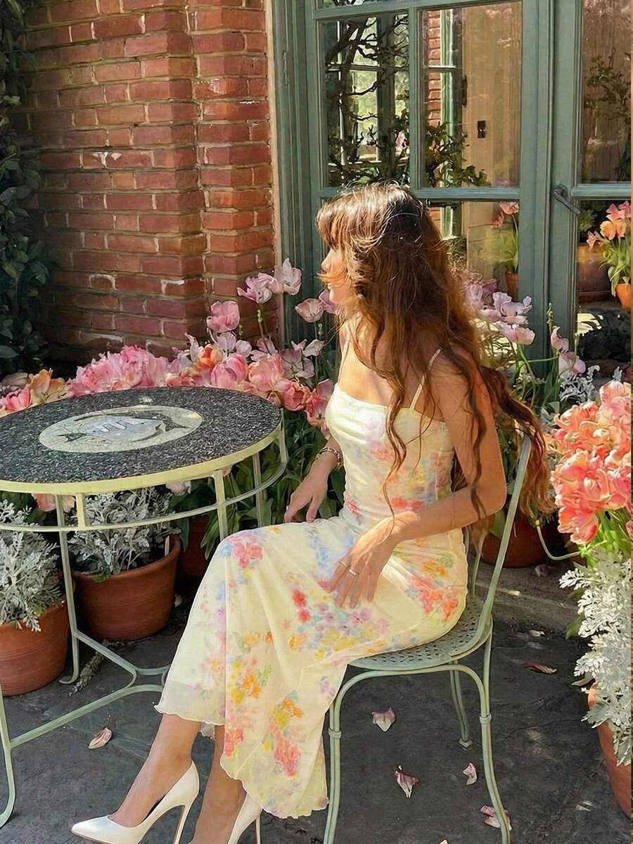 Mujer con vestido largo floral amarillo pastel posando en un jardín de rosas.